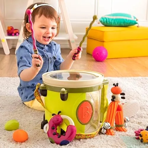 A toddler drums with both sticks, the carrying-strap drum doubling as the storage container.