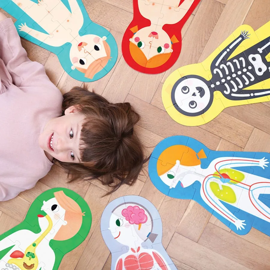 A child lies among the assembled My Body puzzle figures, each piece sized for toddler hands.