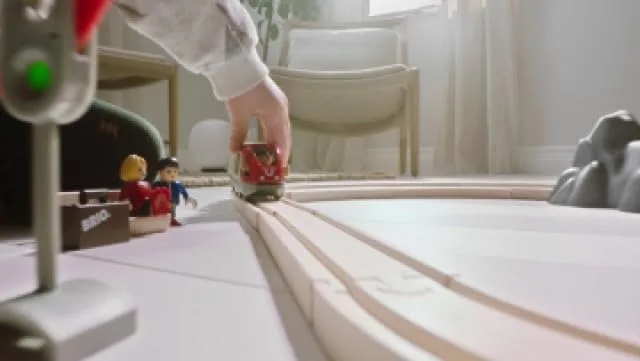 A child's hand guides the BRIO passenger train along the curved wooden track in soft afternoon light