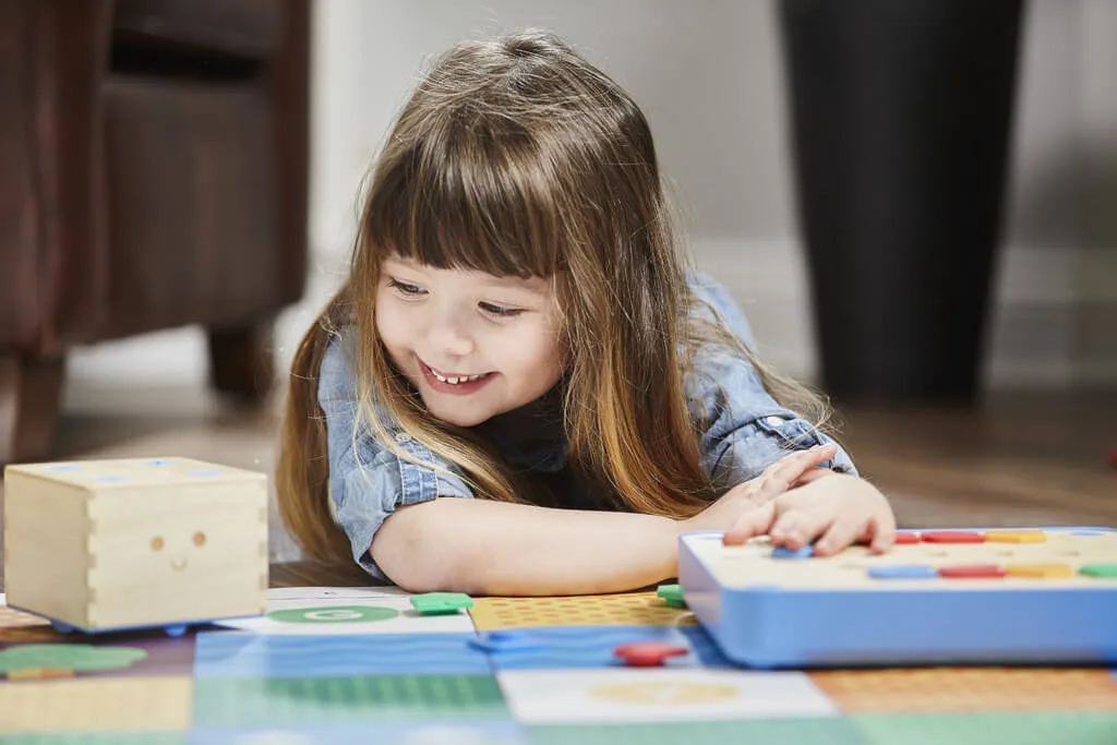 A young coder arranges command tiles on the Cubetto control board, sequencing instructions before pr