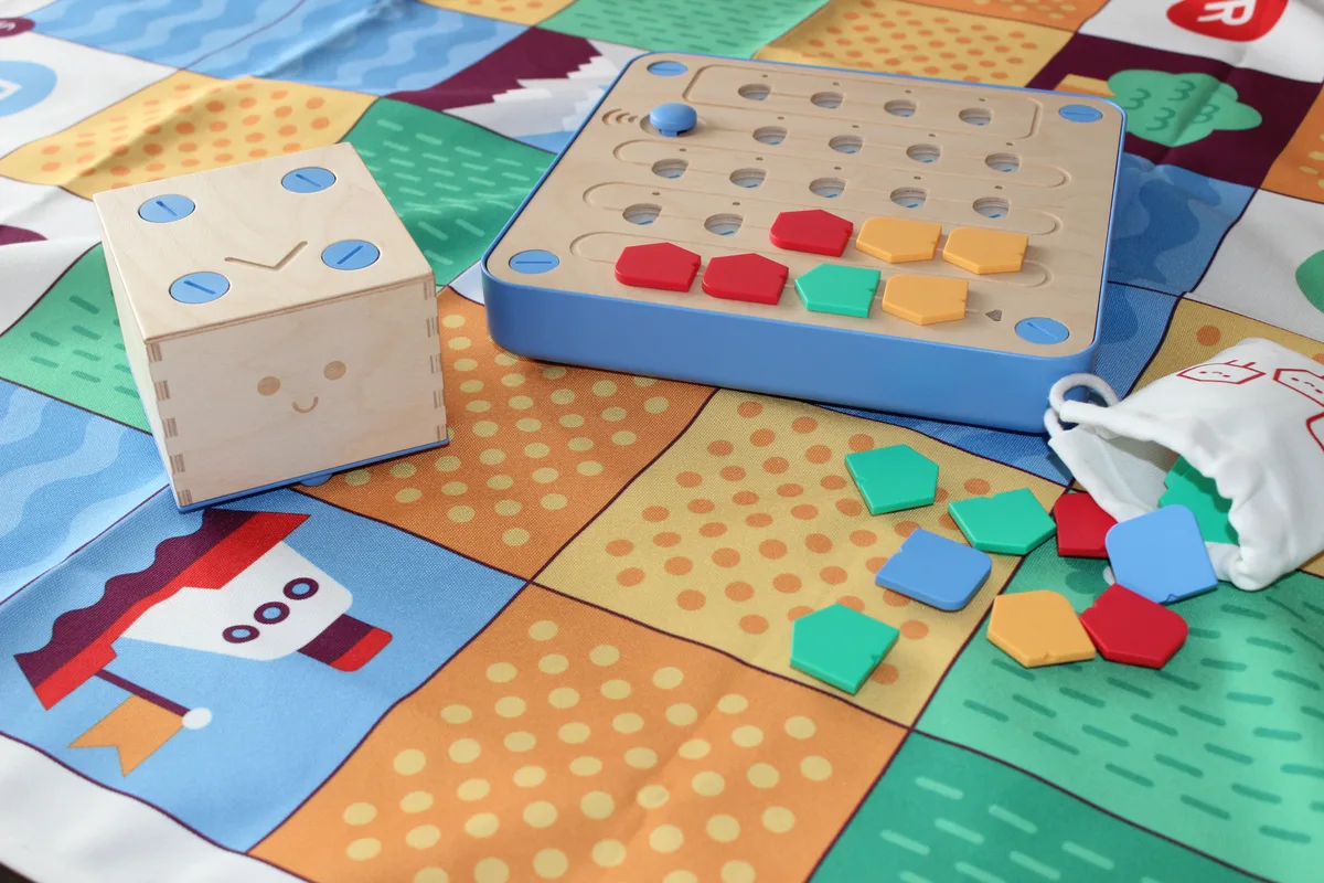 The wooden Cubetto robot, control board, colored command blocks, and adventure mat shown together.