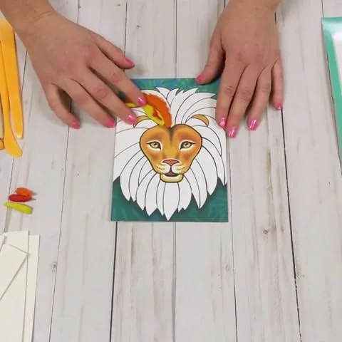 Hands press orange clay onto the lion board, blending sculpting and coloring in a single motion.