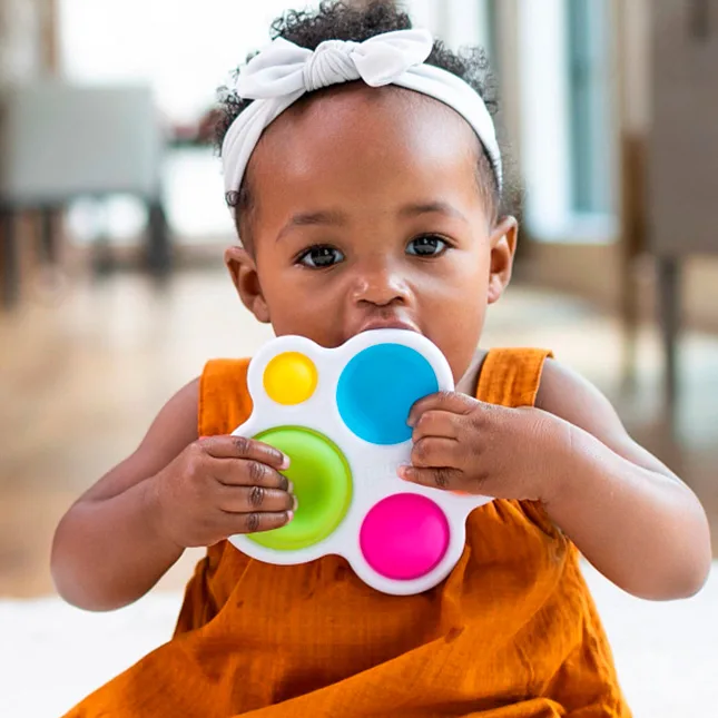 An infant brings the Dimpl to her mouth, exploring its silicone bubbles through every available sens