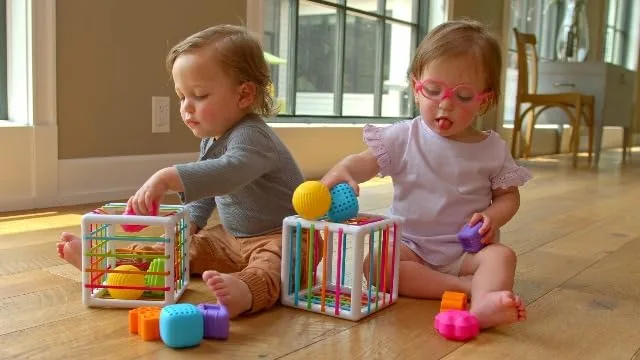 Two toddlers explore InnyBins side by side; the open architecture invites parallel, independent play