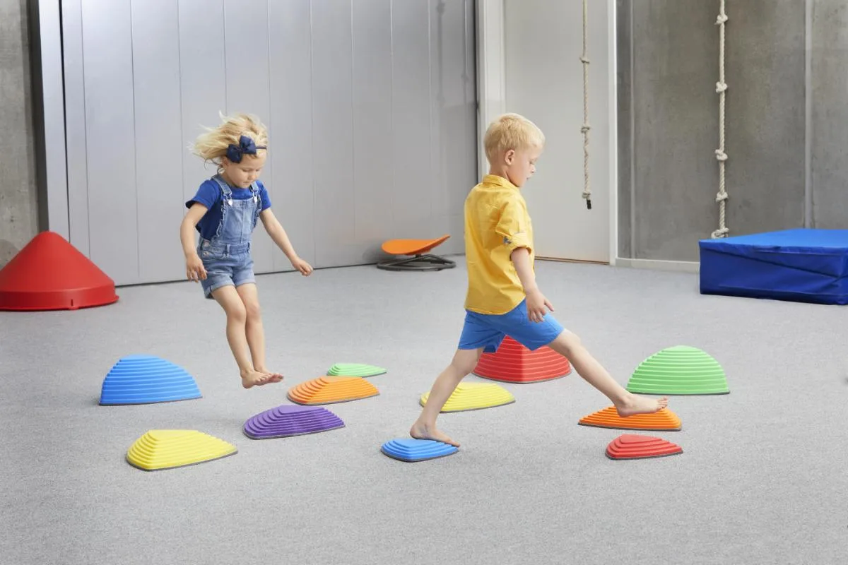 Two children leap and stride between stones, recruiting full-body balance and weight-shift control.