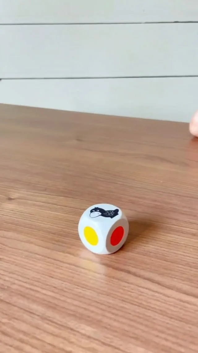 The color die, sized for a toddler's grip, replaces numbers with solid color faces and a raven icon.