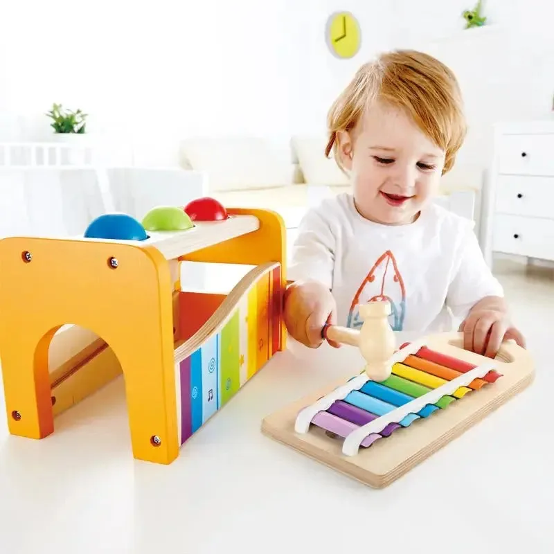 A toddler raises the wooden hammer over a ball, testing the cause-and-effect that anchors this desig