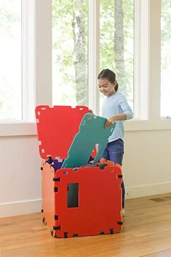 A child mid-build, lifting a panel into place atop an enclosed cube structure.