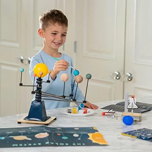 A child paints planets on the assembled solar system model, mid-project at the kitchen table.