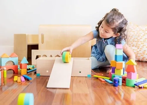 A toddler converts the wooden storage box into a ramp, the integrated-play moment that justifies the