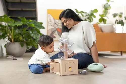A toddler watches the slide-and-seek ball run with a parent — Lovevery's quiet, screen-free aestheti