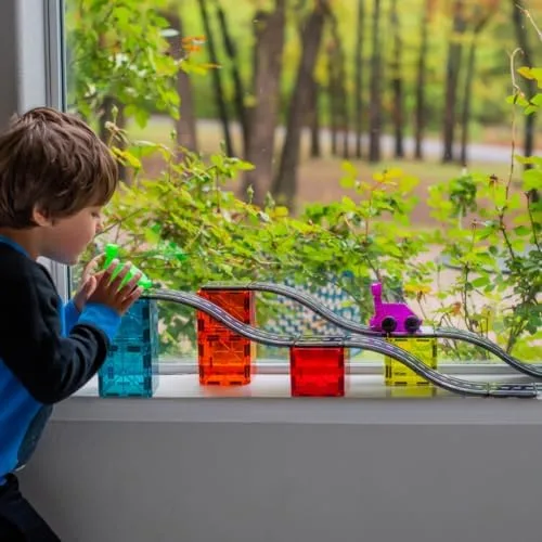 A child tests ramp height on a windowsill build, watching the car descend.