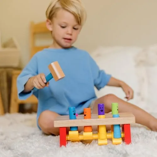 A toddler grips the wooden mallet mid-swing, channeling pounding energy into the pegs.