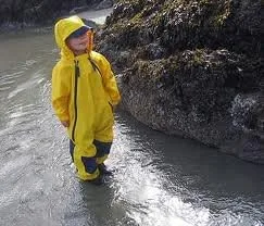 A child wades through cold tidal water, dry underneath because the suit's seams hold.
