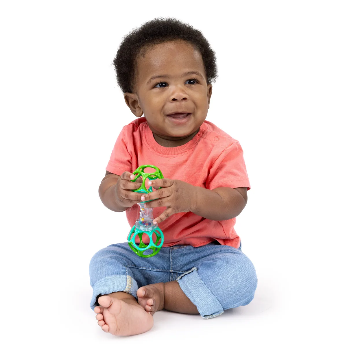 A toddler holds the shaker upright, exploring the contained beads with deliberate two-handed grip.