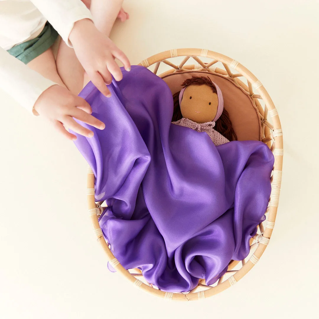 A child tucks a doll into a silk-lined basket, treating the fabric as a soft blanket.