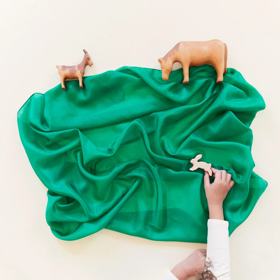 Wooden animals graze across a green silk landscape, the cloth doubling as terrain for figurine play.