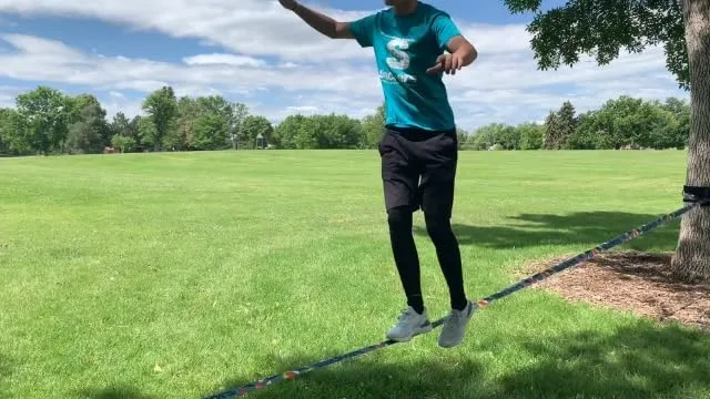 An older child demonstrates a hop on the line — note the soft grass landing zone below.