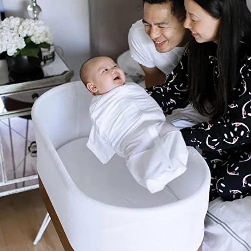 The SNOO at home: parents bend over the bassinet, swaddled newborn inside the proprietary mesh-walle