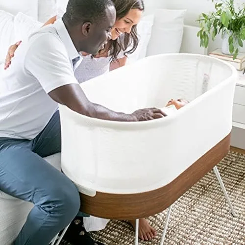 Walnut-and-mesh bassinet on hairpin legs — the design language of premium nursery furniture more tha