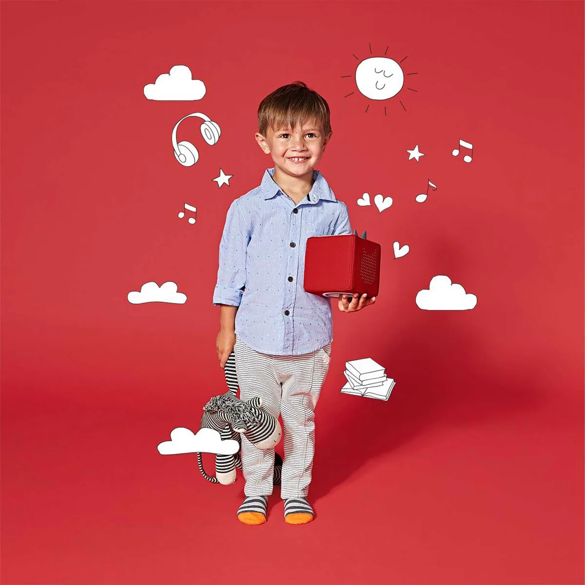 A toddler holds the red Toniebox, a small painted figure within reach for independent play.