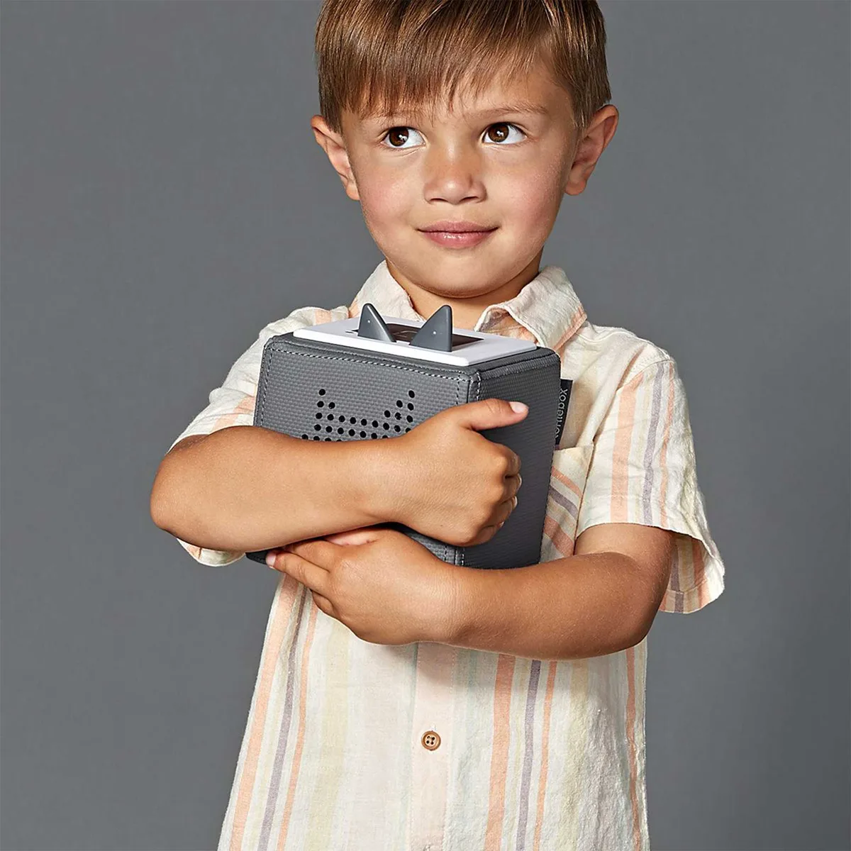 A child cradles the gray Toniebox, the soft fabric edges visible beneath his arms.