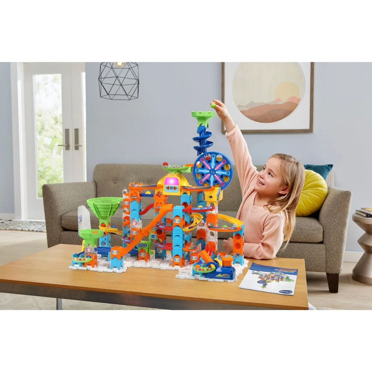 A child loads marbles into the top of the tower in a typical living-room setup.