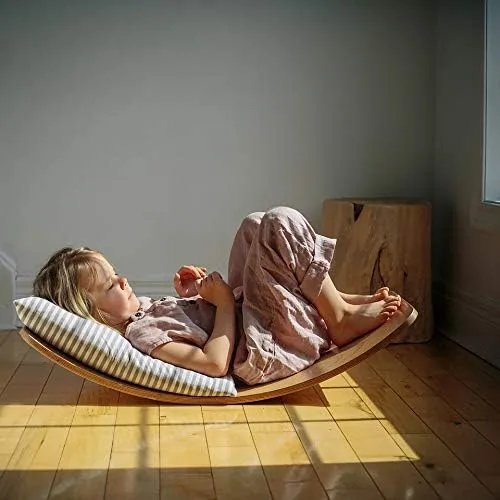 Reclined with a striped pillow, a child uses the gently rocking board as a quiet reading perch.